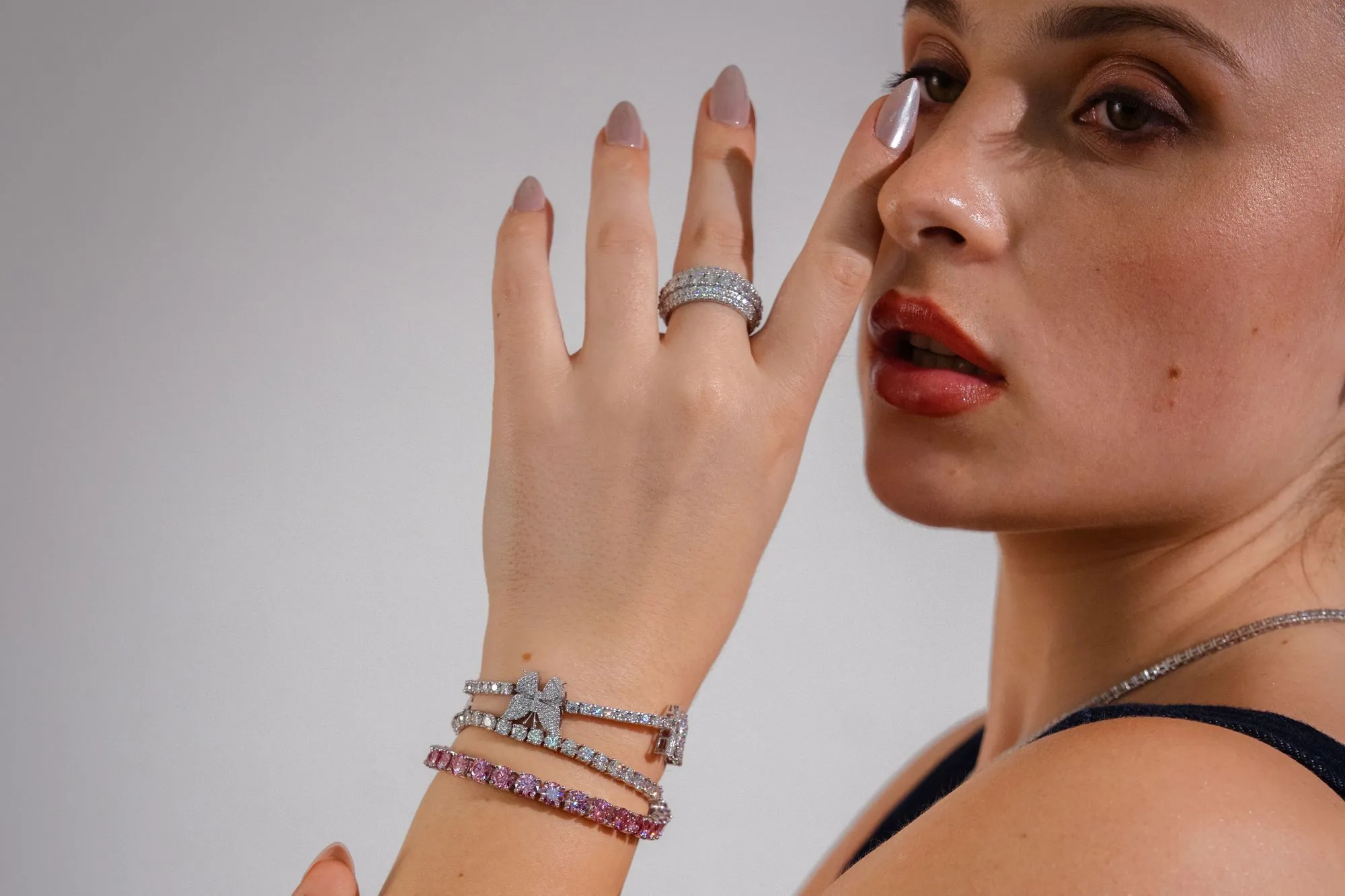 A hand wearing a pavé diamond band and white and pink diamond tennis bracelets